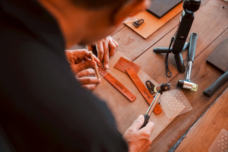 กิจกรรมเวิร์กช็อปทำพวงกุญแจหนัง ISUZU ลงมือทำจริง เวิร์กช็อปทำพวงกุญแจหนัง ISUZU ผู้ร่วมกิจกรรมกำลังตอกอักษรบนแผ่นหนังด้วยมือในบรรยากาศอบอุ่น