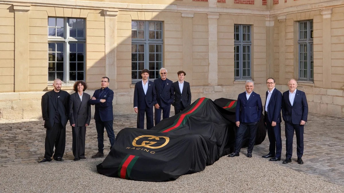 Gucci Racing Alpine Formula One Team ภาพกลุ่มผู้บริหาร ผู้บริหาร Gucci และ Alpine ถ่ายภาพร่วมกับรถแข่งภายใต้ผ้าคลุม Gucci Racing