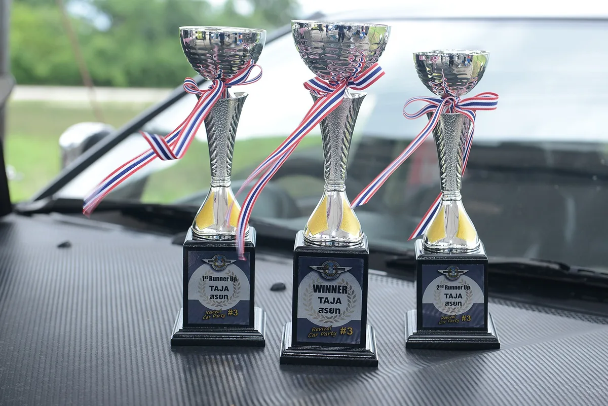 ถ้วยรางวัลสำหรับผู้ชนะกิจกรรม TAJA X Revival Car Party ถ้วยรางวัลการแข่งขัน TAJA X Revival Car Party วางบนฝากระโปรงรถ