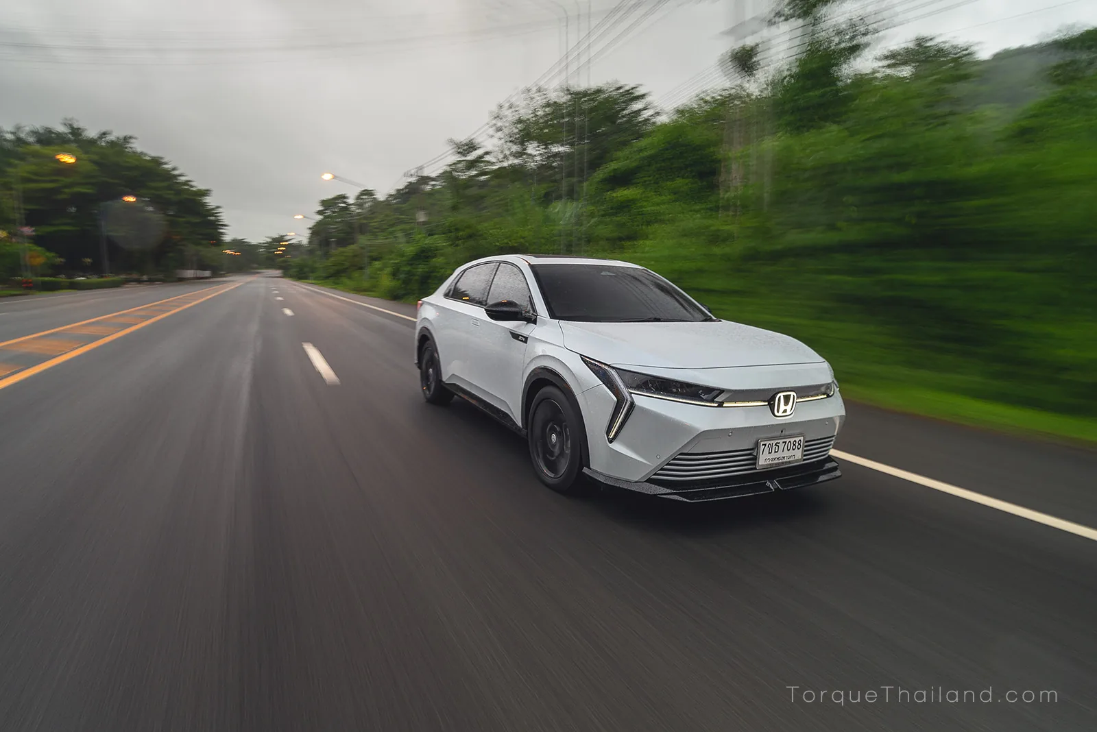 รถยนต์ไฟฟ้า Honda e:N2 เต็มคัน มุมหน้าเฉียง ขณะขับขี่ด้วยความเร็วในโหมด Sport ที่ให้อัตราเร่งทันใจขึ้น พร้อมระบบเสียงสังเคราะห์ทำงานร่วมกับการตัดเสียงภายนอกห้องโดยสาร