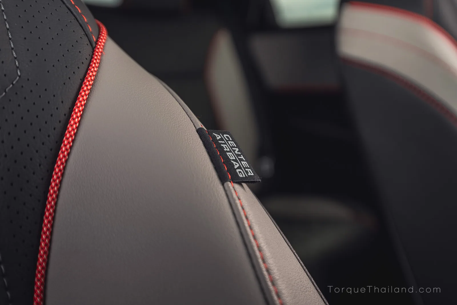 ผ้าระบุข้อความ CENTER AIRBAG ที่ขอบพนักพิงเบาะผู้ขับขี่รถยนต์ไฟฟ้า เพื่อช่วยลดโอกาสบาดเจ็บจากการกระแทกกันระหว่างผู้นั่งเบาะหน้า