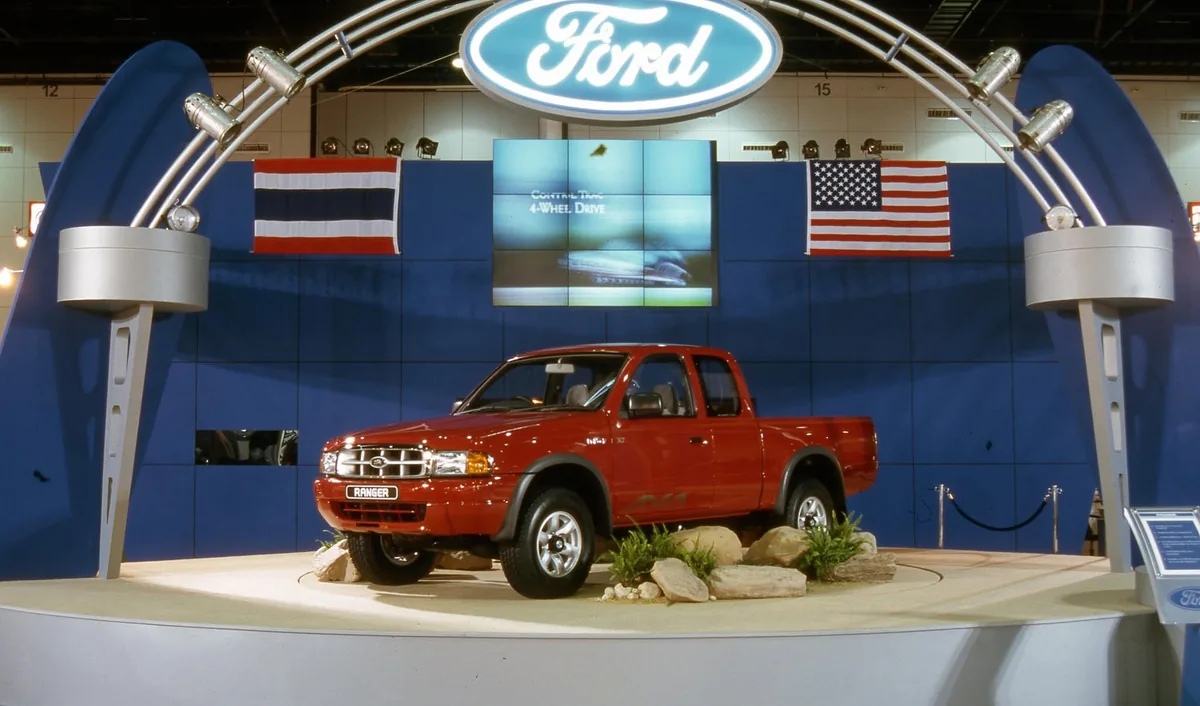 Ford Ranger Open Cab เปิดตัวปี 1998 Ford Ranger Open Cab สีแดงในงานเปิดตัวปี 1998 พร้อมโลโก้ Ford และธงไทยกับสหรัฐอเมริกา