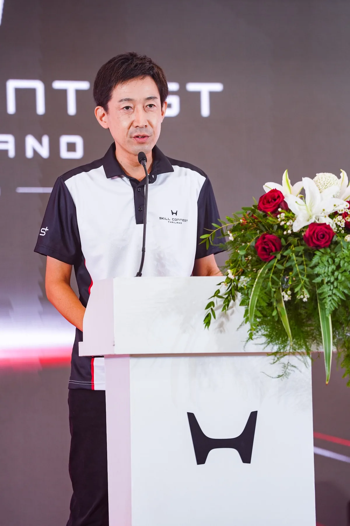 ผู้บริหารกล่าวบนเวที Honda Skill Contest ผู้บริหารกำลังกล่าวบนเวทีในการแข่งขัน Honda Skill Contest Thailand ที่โพเดียมพร้อมช่อดอกไม้