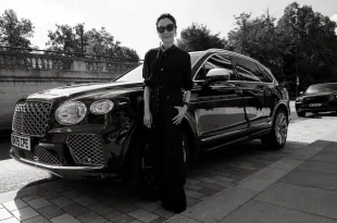 มิเชล โหย่ว (Michelle Yeoh) สวมแว่นกันแดดยืนอยู่ด้านหน้ารถยนต์ SUV สีดำของ Bentley ในภาพขาวดำ