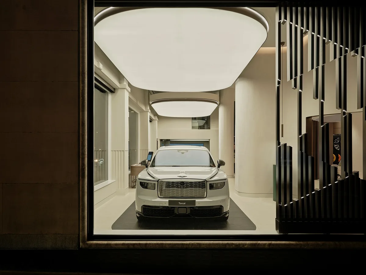 รถ Bentley สีขาวมุมด้านหน้าผ่านกระจกโชว์รูม รถยนต์ Bentley สีขาวมุมด้านหน้า มองผ่านกระจกโชว์รูมที่มีองค์ประกอบตกแต่งแนวตั้ง