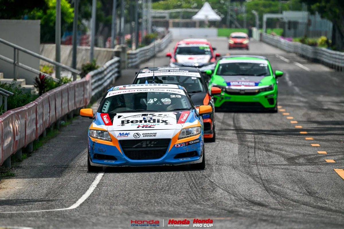 กลุ่มรถแข่ง Honda One Make Race ในสนาม รถแข่ง Honda หมายเลข 23 นำกลุ่มรถแข่งบนถนนที่มีแบริเออร์กั้นสองข้างในสนามสงขลา