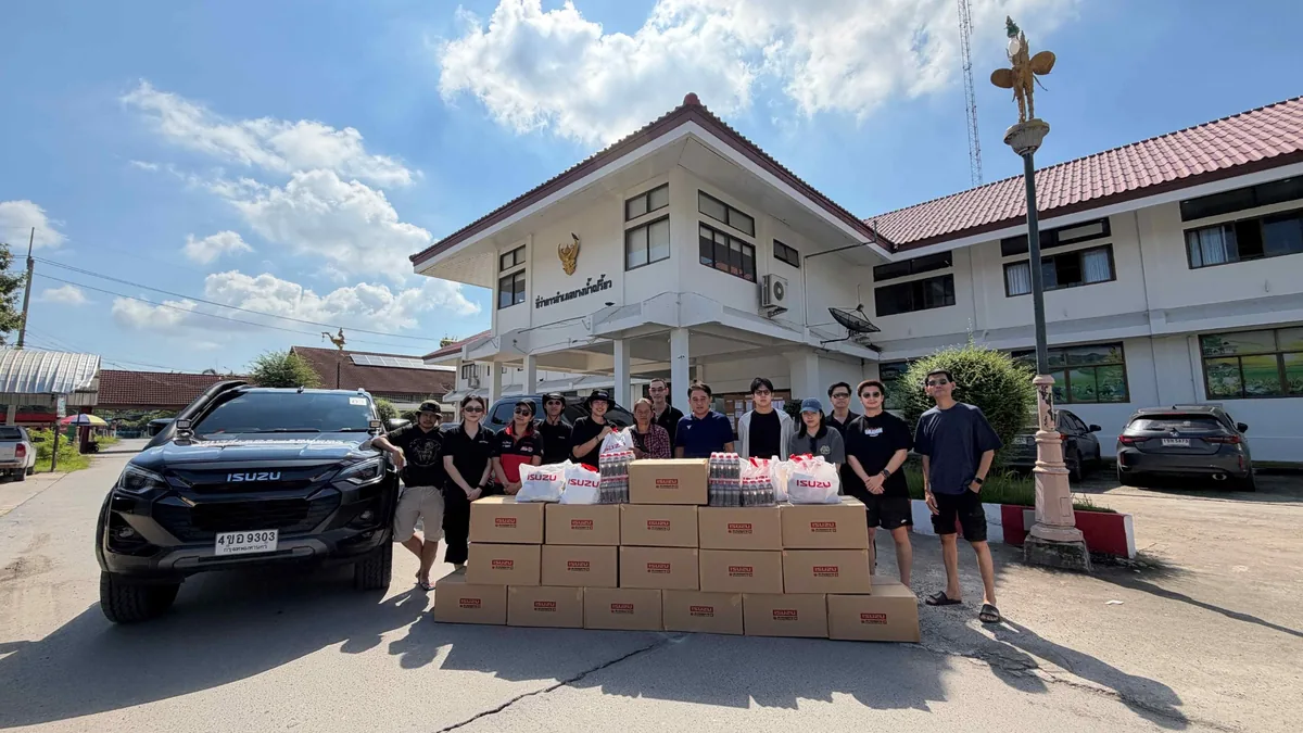 อีซูซุส่งมอบสิ่งของช่วยเหลือผู้ประสบภัยน้ำท่วม กลุ่มผู้ร่วมส่งมอบสิ่งของช่วยเหลือน้ำท่วมยืนด้านหลังกล่องสิ่งของ น้ำดื่ม และถุงอีซูซุ โดยมีรถอีซูซุจอดด้านข้าง