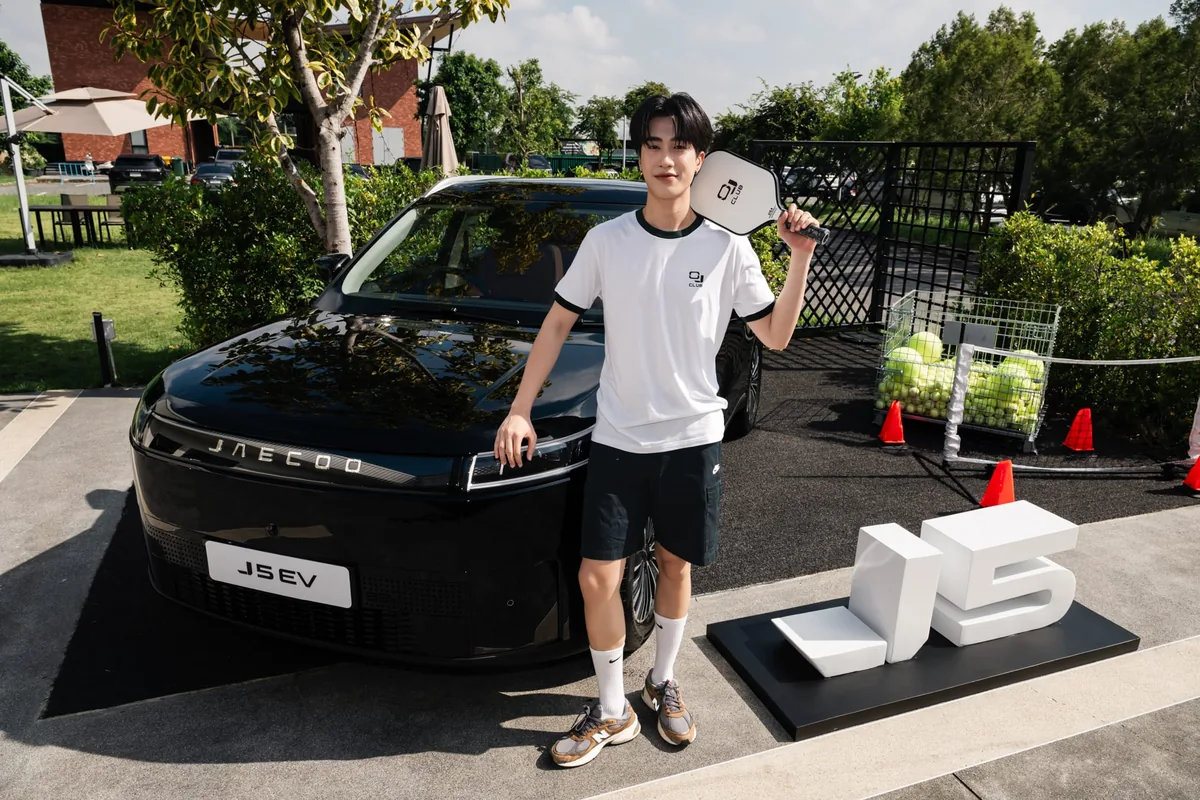 JAECOO 5 EV กับกิจกรรมกีฬา OJ CLUB ผู้ร่วมงาน OJ CLUB ถือไม้กีฬา Padel ยืนข้างรถยนต์ไฟฟ้า JAECOO 5 EV สีดำ พร้อมป้าย J5 และลูกบอลกีฬา