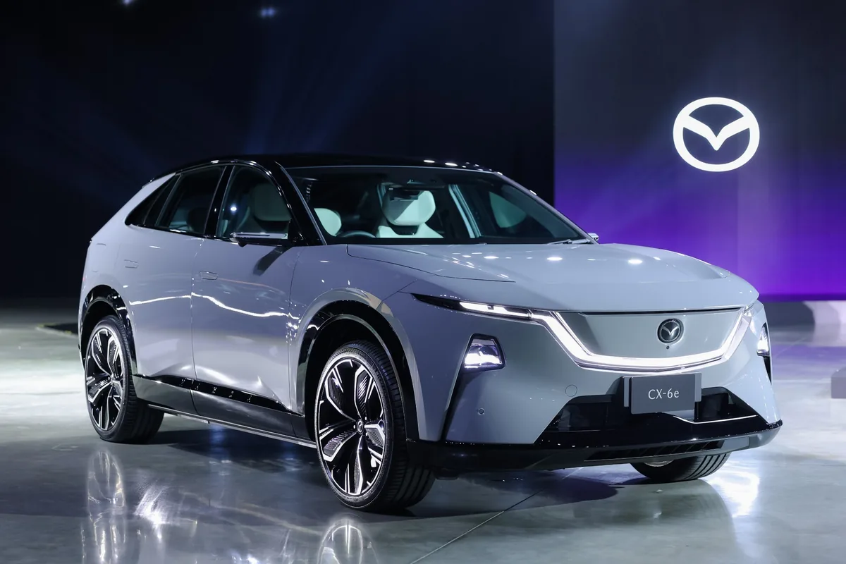 Mazda CX-6e รุ่น Premium Sports Mazda CX-6e ตัวถังสีอ่อนมุมหน้าสามส่วน พร้อมโลโก้ Mazda บนฉากหลัง
