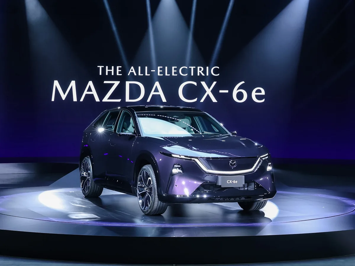 Mazda CX-6e รุ่น Premium Sports สี Nightfall Violet / Jet Black Mazda CX-6e สีม่วง มุมเฉียงด้านหน้าบนเวที พร้อมข้อความชื่อรุ่นด้านหลัง