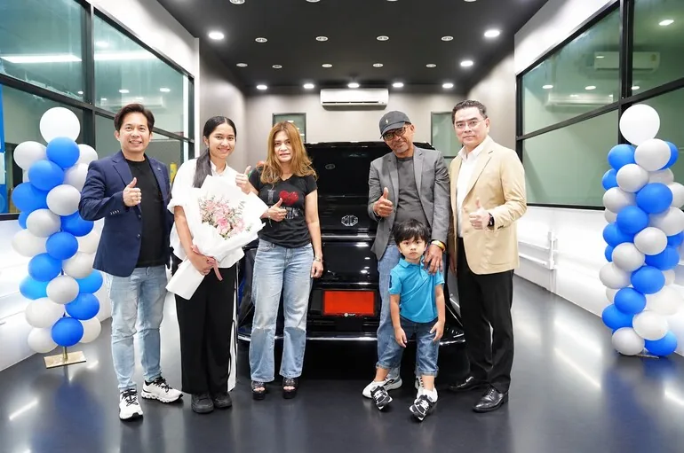 เนเน่ รอยัล และครอบครัวกับ MG MAXUS 9 V PLUS เนเน่ รอยัล และกลุ่มผู้ร่วมถ่ายภาพยืนหน้ารถ MG MAXUS 9 V PLUS สีดำ พร้อมช่อดอกไม้ภายในอาคาร
