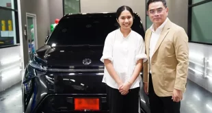 เนเน่ รอยัล ยืนคู่กับผู้ร่วมถ่ายภาพด้านหน้ารถยนต์ MG MAXUS 9 V PLUS สีดำ ภายในอาคาร