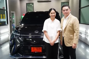 เนเน่ รอยัล ยืนคู่กับผู้ร่วมถ่ายภาพด้านหน้ารถยนต์ MG MAXUS 9 V PLUS สีดำ ภายในอาคาร