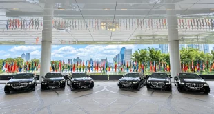 รถยนต์ BMW สีเข้ม 6 คันจอดเรียงกันใต้หลังคาอาคาร โดยมีธงนานาชาติอยู่ด้านหลัง