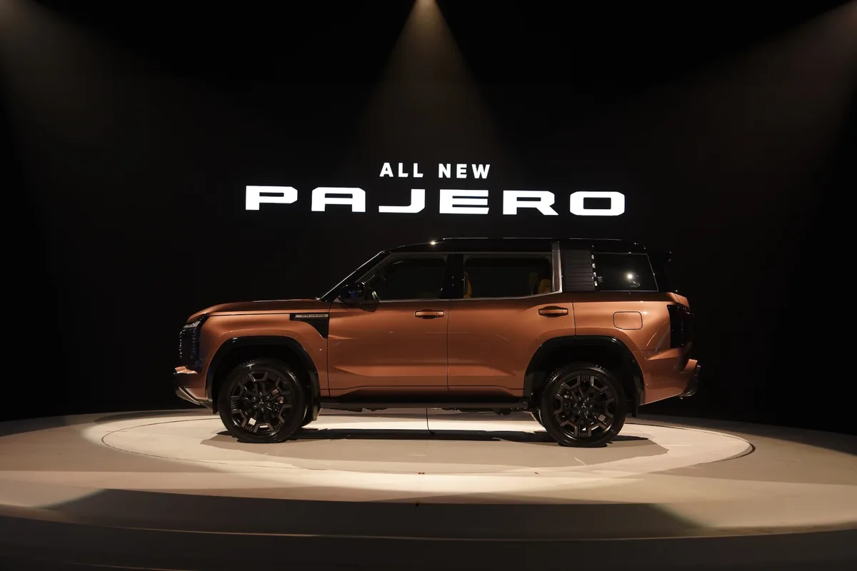 Mitsubishi Pajero Super Exceed 4WD มุมด้านข้าง All-New Mitsubishi Pajero Super Exceed 4WD ตัวถังสีทองแดง มุมด้านข้างบนแท่นจัดแสดง พร้อมป้าย ALL NEW PAJERO ด้านหลัง