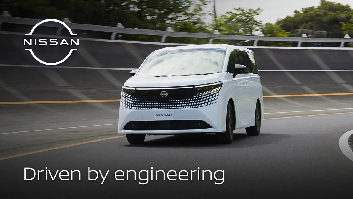 Nissan Elgrand e-POWER มุมหน้าขณะวิ่ง Nissan Elgrand e-POWER สีขาวขณะวิ่งบนถนน มุมด้านหน้า พร้อมโลโก้ Nissan และข้อความ Driven by engineering