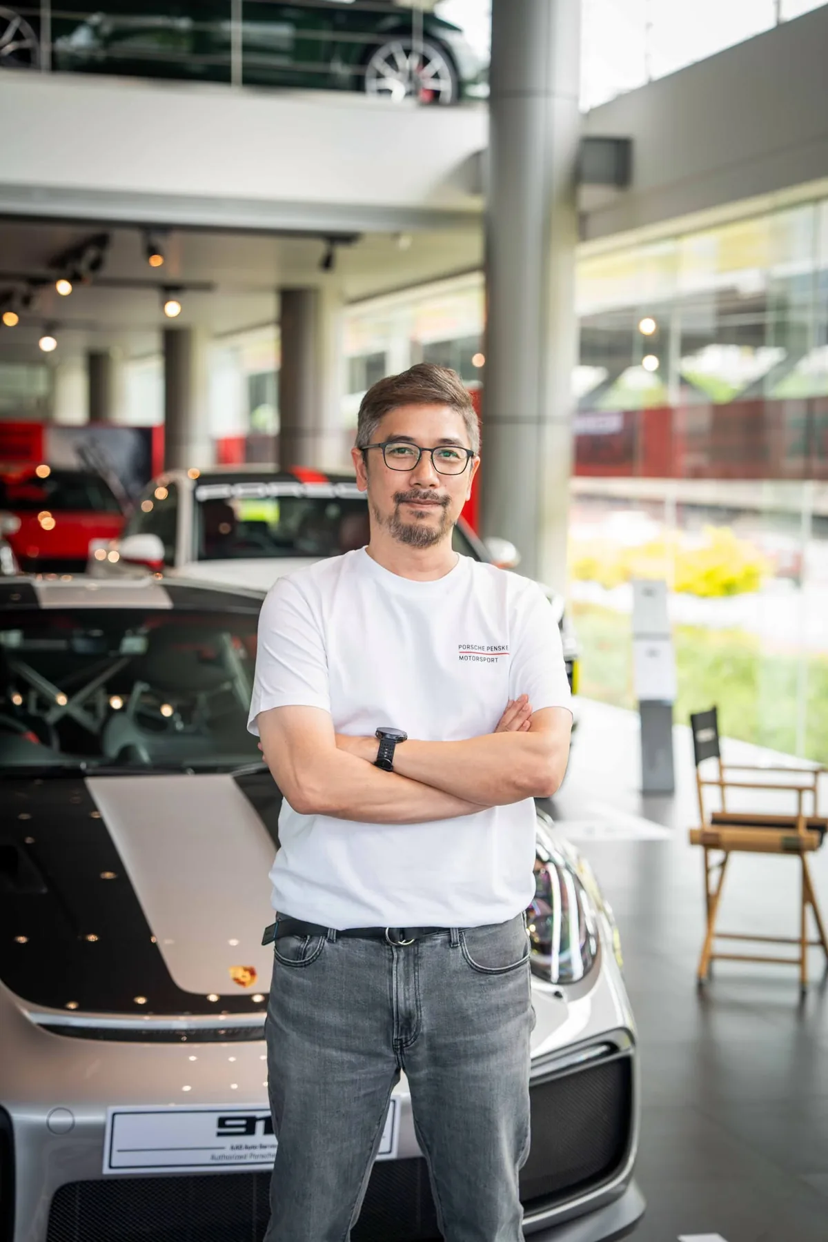 นายทิวนาถ รังสิพราหมณกุล – Porsche AAS นายทิวนาถ รังสิพราหมณกุล ยืนด้านหน้ารถ Porsche ภายในโชว์รูม