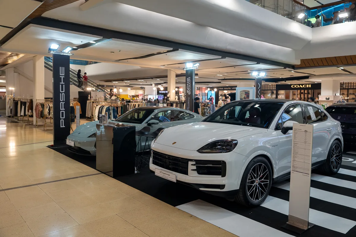 Porsche Cayenne S E-Hybrid Coupé ภายในงาน Roadshow Porsche Cayenne S E-Hybrid Coupé สีขาวจัดแสดงภายในงาน Porsche AAS Roadshow โดยมีรถ Porsche Taycan อยู่ด้านหลัง
