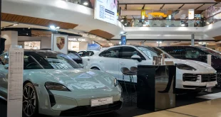 Porsche Taycan Turbo สีเขียวอ่อนด้านหน้าและ Cayenne S E-Hybrid Coupé สีขาวด้านหลังภายในพื้นที่จัดแสดงของ Porsche AAS