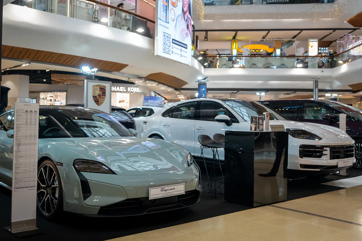 Porsche Taycan Turbo และ Cayenne ในงาน AAS Roadshow Porsche Taycan Turbo สีเขียวอ่อนด้านหน้าและ Cayenne S E-Hybrid Coupé สีขาวด้านหลังภายในพื้นที่จัดแสดงของ Porsche AAS