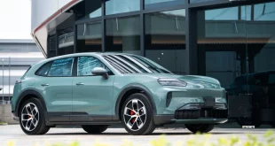 รถยนต์ Porsche SUV สีเขียวอ่อน มุมด้านหน้าเฉียง จอดอยู่หน้าอาคารกระจก