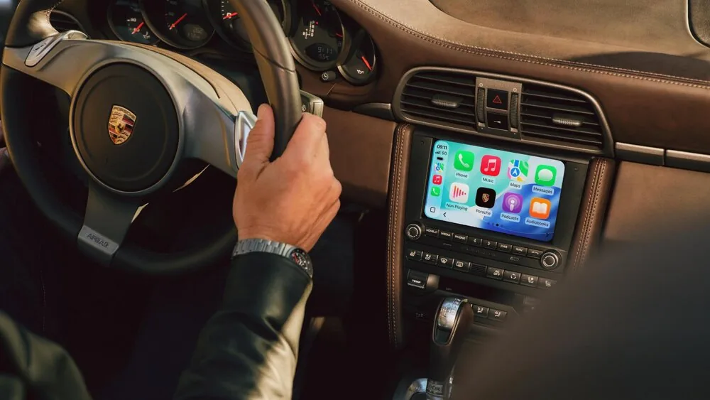 Porsche PCCM Plus แสดง Apple CarPlay Apple CarPlay บนหน้าจอ PCCM Plus ที่ติดตั้งในคอนโซล Porsche พร้อมพวงมาลัยและผู้ขับขี่