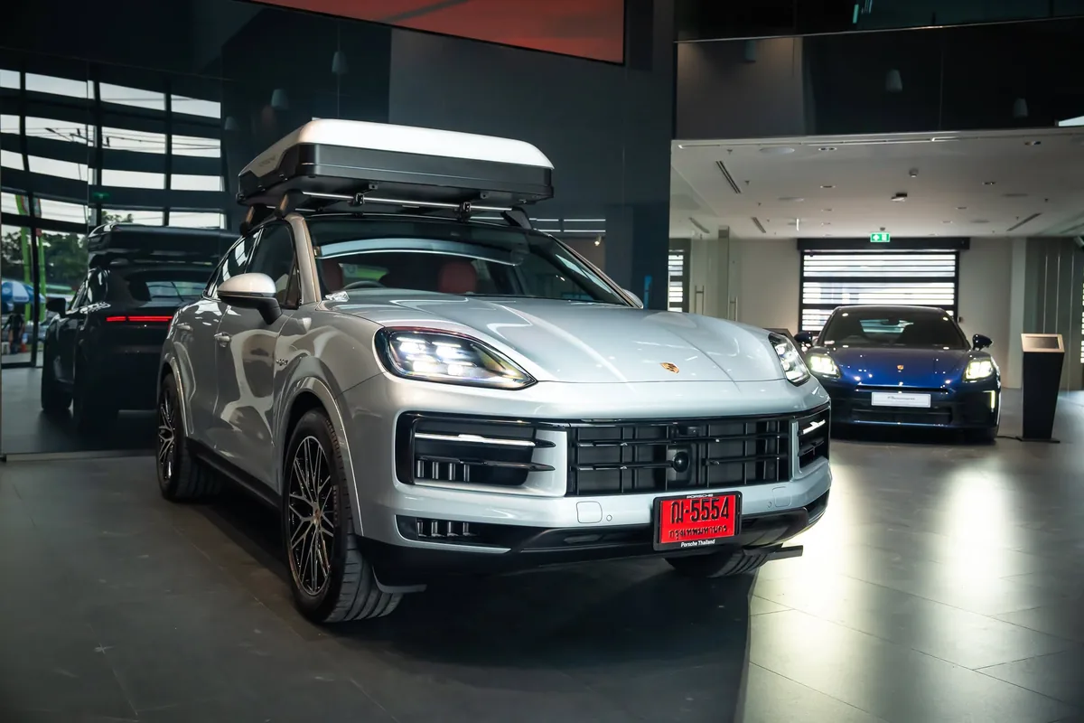 Porsche SUV สีเงินพร้อมกล่องสัมภาระบนหลังคา Porsche SUV สีเงินพร้อมกล่องสัมภาระบนหลังคา จอดภายในโชว์รูม มีรถ Porsche สีอื่นอยู่ด้านหลัง