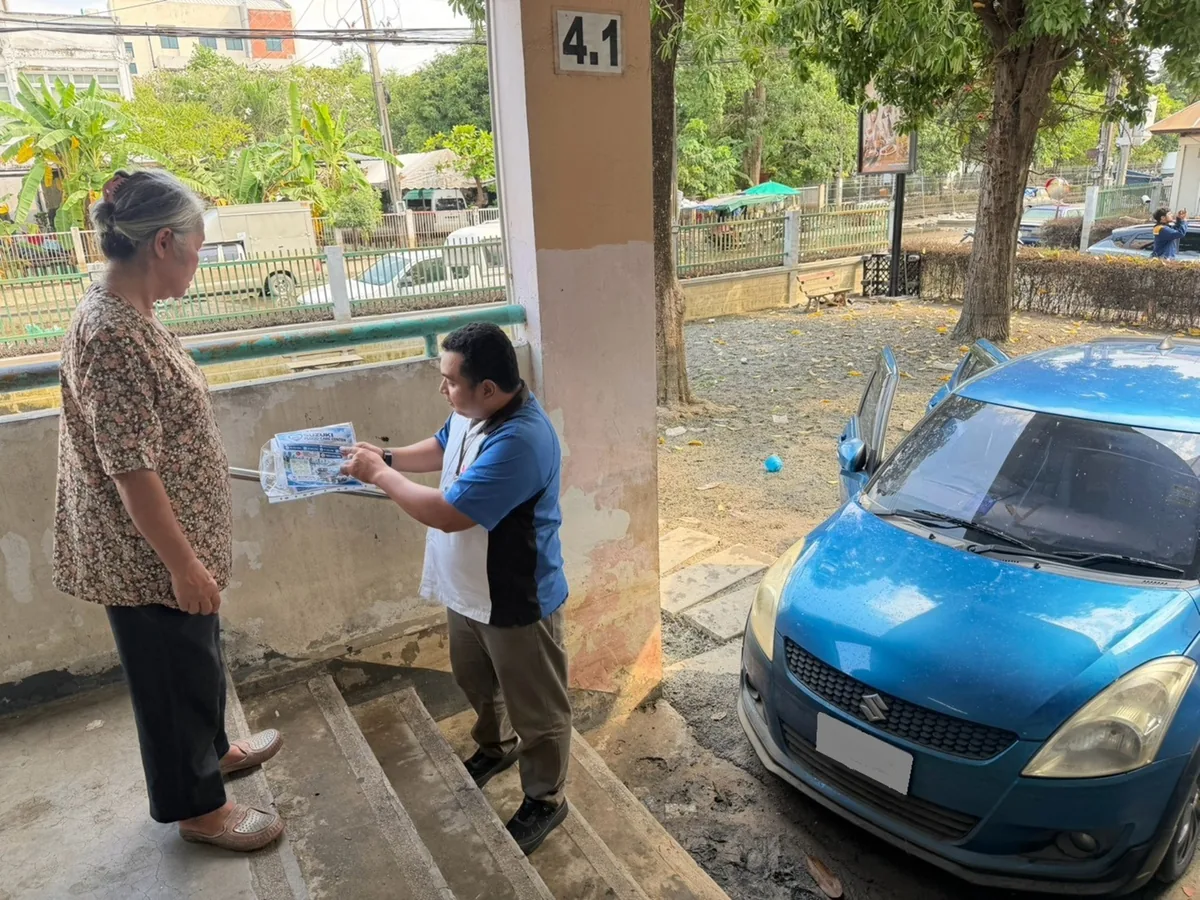 ทีม Suzuki Flood Hunter พบเจ้าของรถ Suzuki เจ้าหน้าที่ซูซูกิอธิบายเอกสารให้ผู้หญิงข้างรถ Suzuki สีน้ำเงินที่จอดอยู่ริมอาคาร