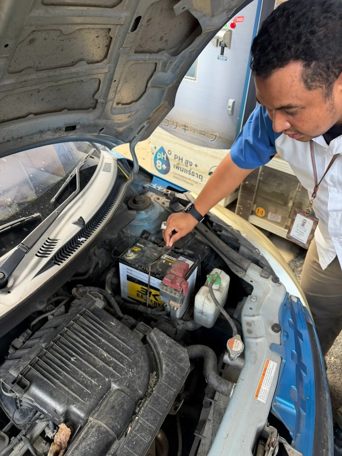 เจ้าหน้าที่ Suzuki ตรวจสอบแบตเตอรี่รถยนต์ เจ้าหน้าที่ซูซูกิก้มตรวจสอบบริเวณแบตเตอรี่ในห้องเครื่องรถยนต์ที่เปิดฝากระโปรง