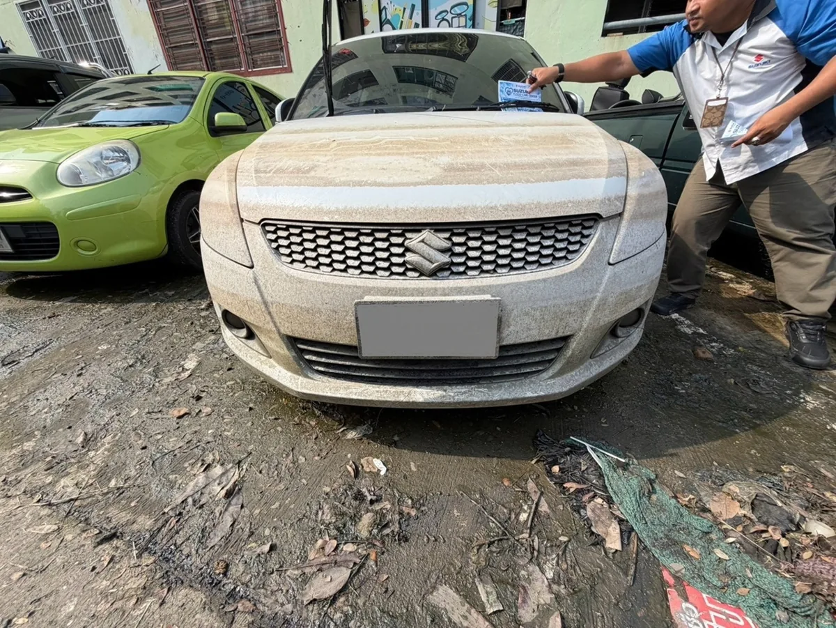 ทีม Suzuki Flood Hunter ลงพื้นที่ติดเอกสารแจ้งข้อมูล รถ Suzuki สีอ่อนมีคราบฝุ่นบนตัวถัง ขณะเจ้าหน้าที่วางเอกสารประชาสัมพันธ์บนกระจกหน้า