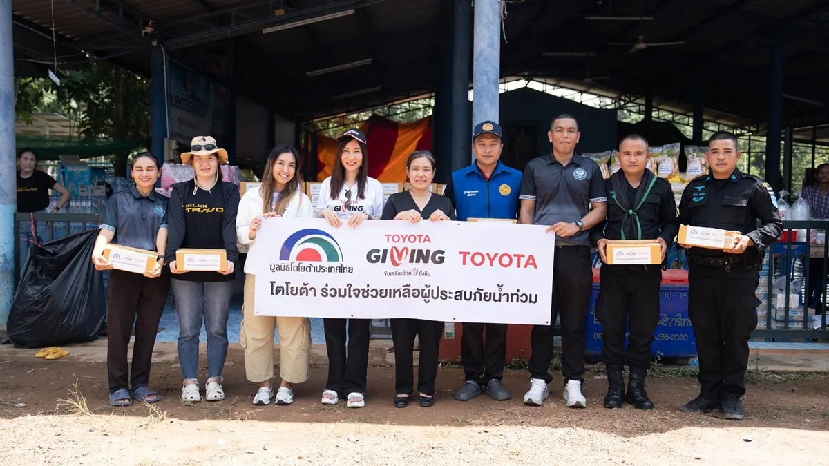 โตโยต้าส่งมอบกล่องช่วยเหลือผู้ประสบภัยน้ำท่วม กลุ่มผู้ร่วมกิจกรรมโตโยต้าถือกล่องสิ่งของและป้ายช่วยเหลือผู้ประสบภัยน้ำท่วมที่จุดส่งมอบ
