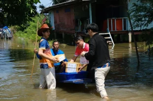 ผู้ร่วมกิจกรรมช่วยกันขนย้ายกล่องสิ่งของลงเรือในบริเวณชุมชนที่มีน้ำท่วมขัง
