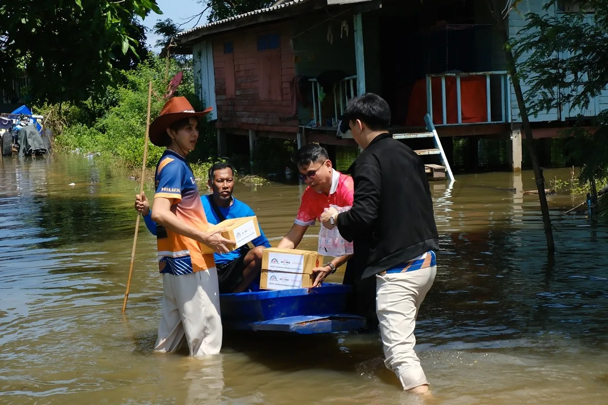 การขนส่งสิ่งของช่วยเหลือในชุมชนน้ำท่วม ผู้ร่วมกิจกรรมช่วยกันขนย้ายกล่องสิ่งของลงเรือในบริเวณชุมชนที่มีน้ำท่วมขัง