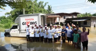 ผู้ร่วมกิจกรรม TOYOTA GIVING และประชาชนยืนร่วมกันในพื้นที่น้ำท่วมข้างรถช่วยเหลือ