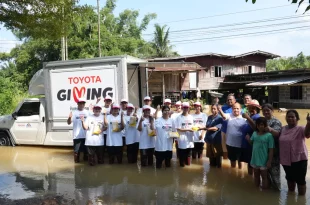 ผู้ร่วมกิจกรรม TOYOTA GIVING และประชาชนยืนร่วมกันในพื้นที่น้ำท่วมข้างรถช่วยเหลือ