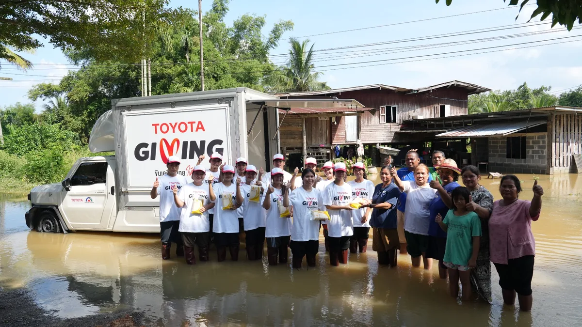 TOYOTA GIVING ช่วยเหลือผู้ประสบอุทกภัย ผู้ร่วมกิจกรรม TOYOTA GIVING และประชาชนยืนร่วมกันในพื้นที่น้ำท่วมข้างรถช่วยเหลือ