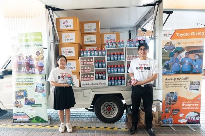จุดแสดงอุปกรณ์ดูแลสุขภาพช่องปาก Toyota Giving ผู้ร่วมกิจกรรมสองคนยืนหน้ารถจัดแสดงผลิตภัณฑ์ดูแลสุขภาพช่องปากและป้าย Toyota Giving