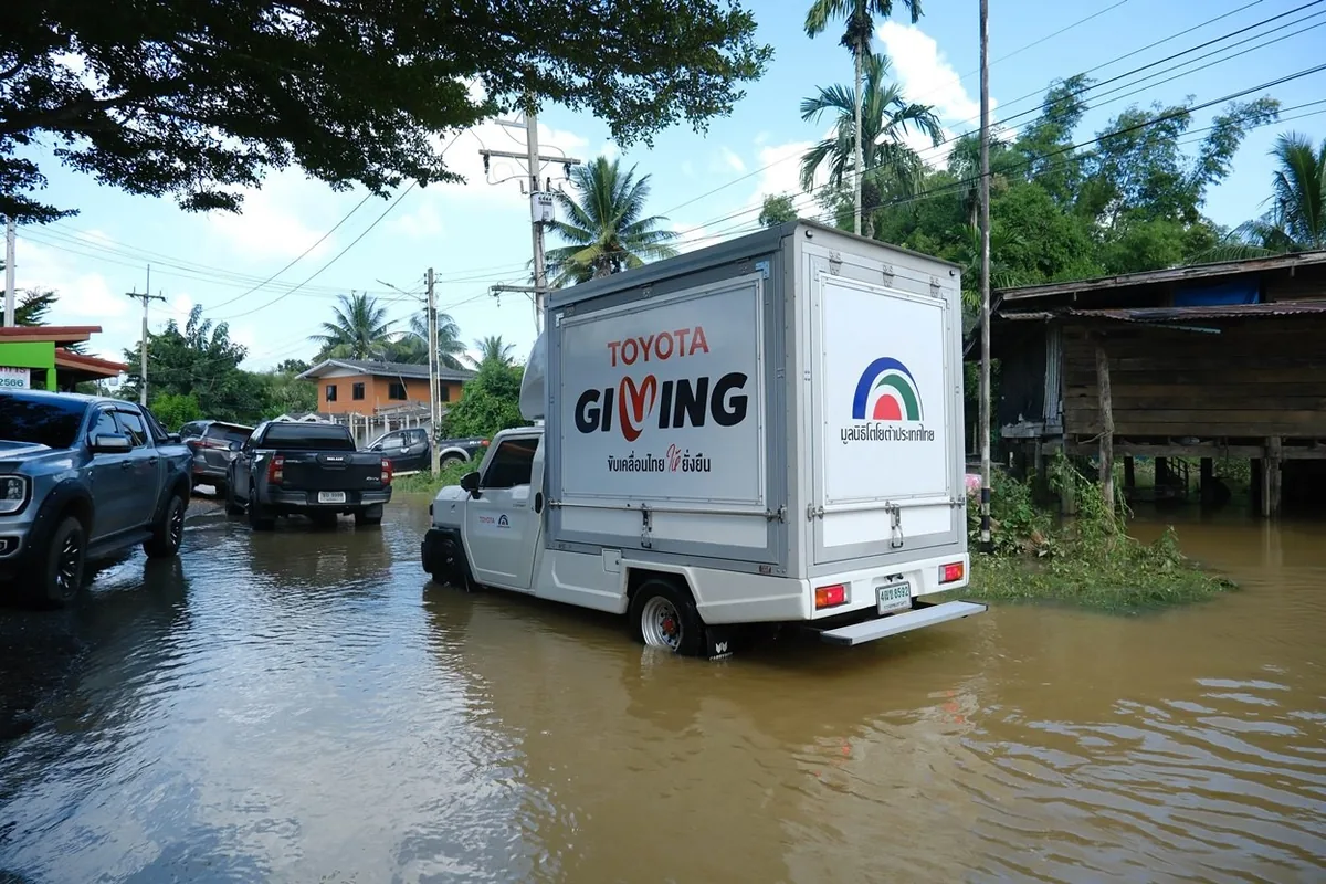 รถขนส่ง TOYOTA GIVING บนถนนน้ำท่วม รถขนส่งติดสัญลักษณ์ TOYOTA GIVING และมูลนิธิโตโยต้าประเทศไทย เดินทางบนถนนที่มีน้ำท่วมขัง